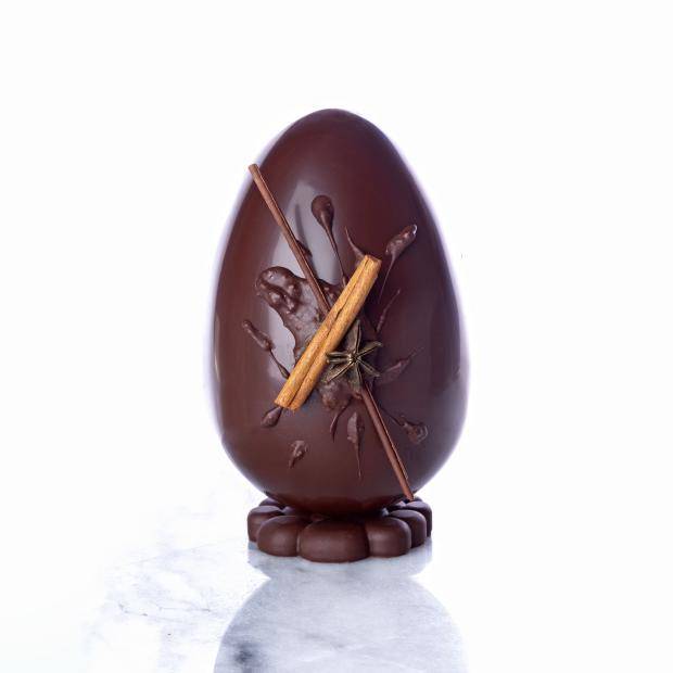 ovo de chocolate escuro em pé de frente com pedaço de canela em pau na frente